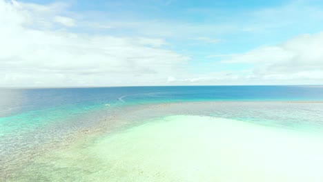 Horizont-Drohnenaufnahme-Von-Türkisfarbenem-Schwalbenwasser-Im-Tropischen-Pazifischen-Ozean-Unter-Blauem-Himmel-Und-Weißen-Wolken,-Die-über-Weißen-Sand-Und-Korallen-Fliegen