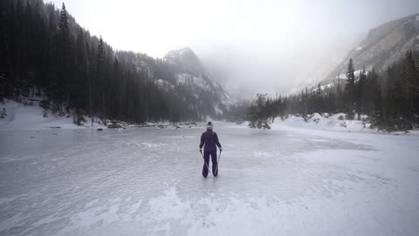 female hiker walking on snow and ice of frozen lake in cold winter day