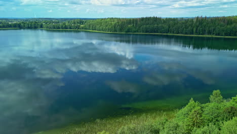 Flying-over-a-lake-with-clear-water-which-is-situated-between-the-needle-forest-and-mirroring-the-sky-above-it