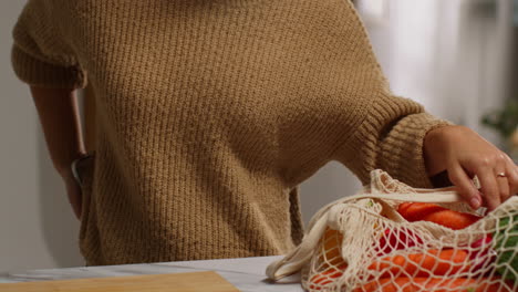 woman talking on mobile phone getting home from food shopping unpacking bag of fresh vegetables onto counter in kitchen