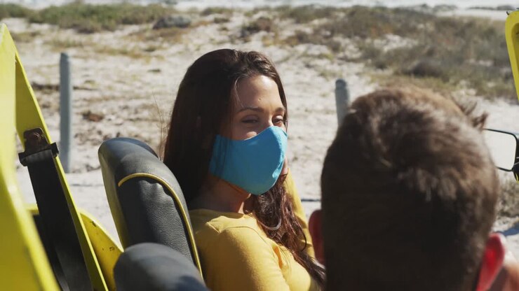 Felice coppia caucasica con mascherine seduta in un buggy da spiaggia.