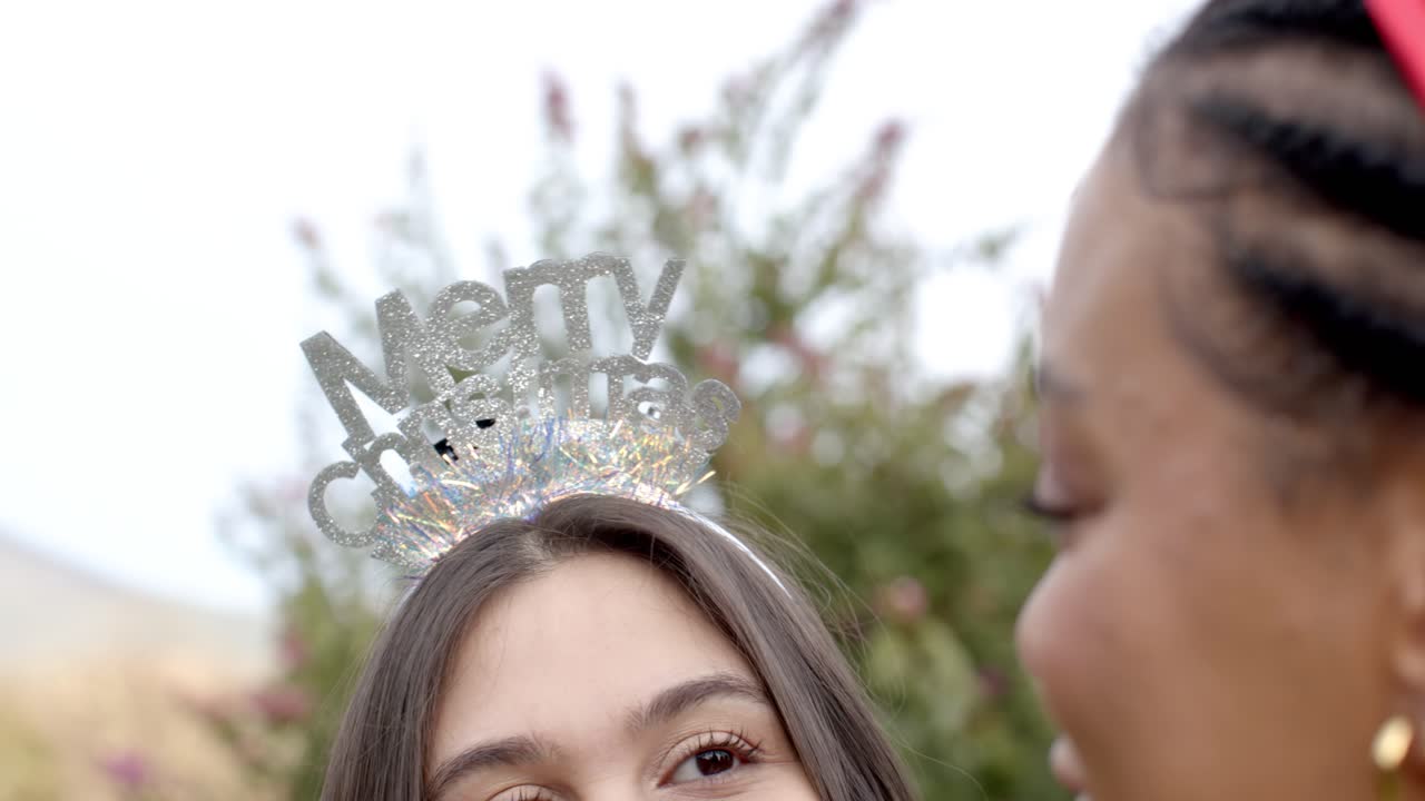 Pergeseran kamera memperlihatkan bando Natal pada anak perempuan saat ibu dan anak perempuan yang berbeda latar belakang bertukar pandang di halaman.