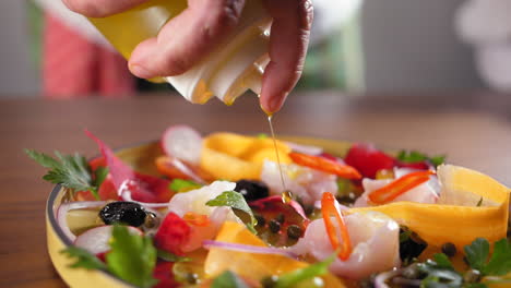 chef with a white shirt prepares a sea bass carpaccio and puts olive oil on it -close up slow motion shot