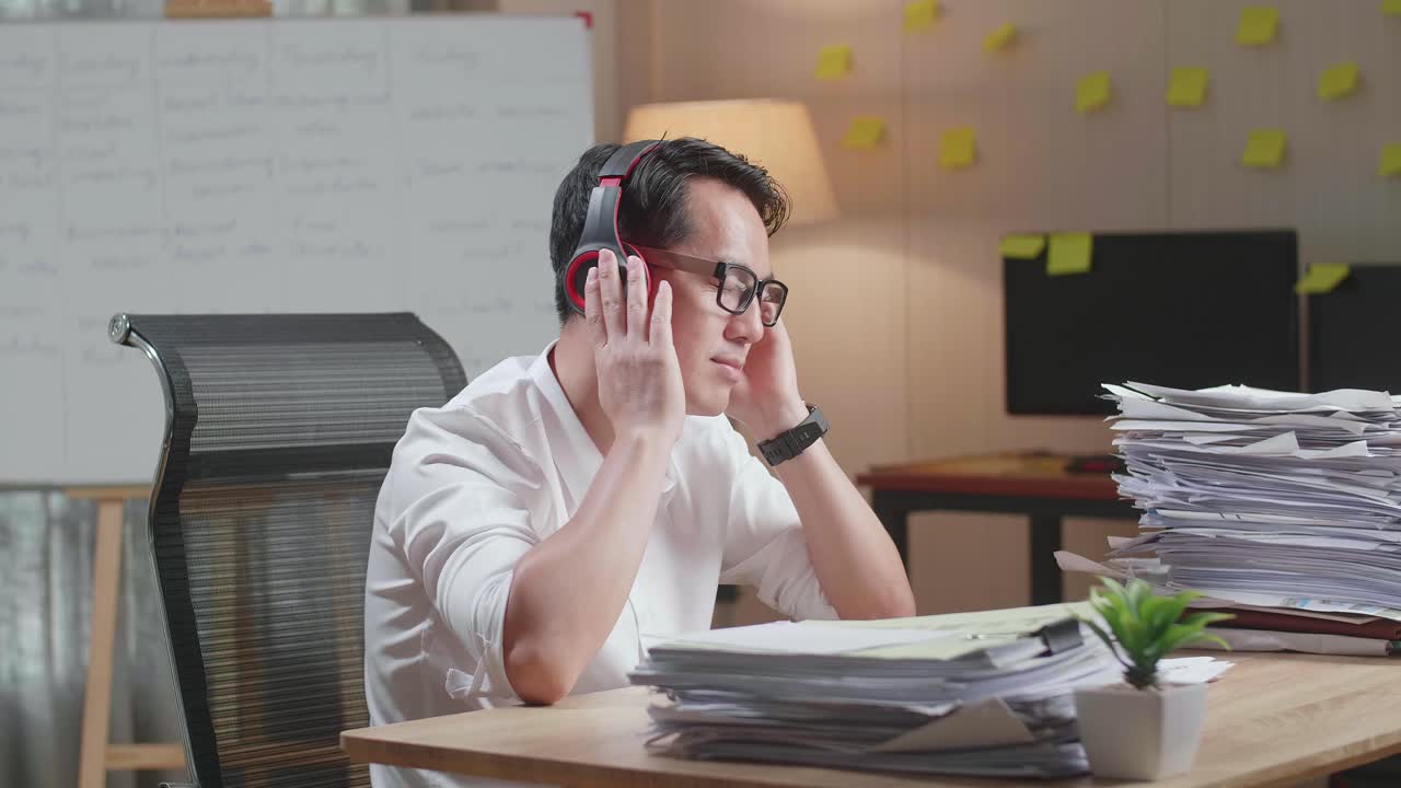 hombre asiático usando auriculares para escuchar música y bailar después de trabajar con documentos en la oficina