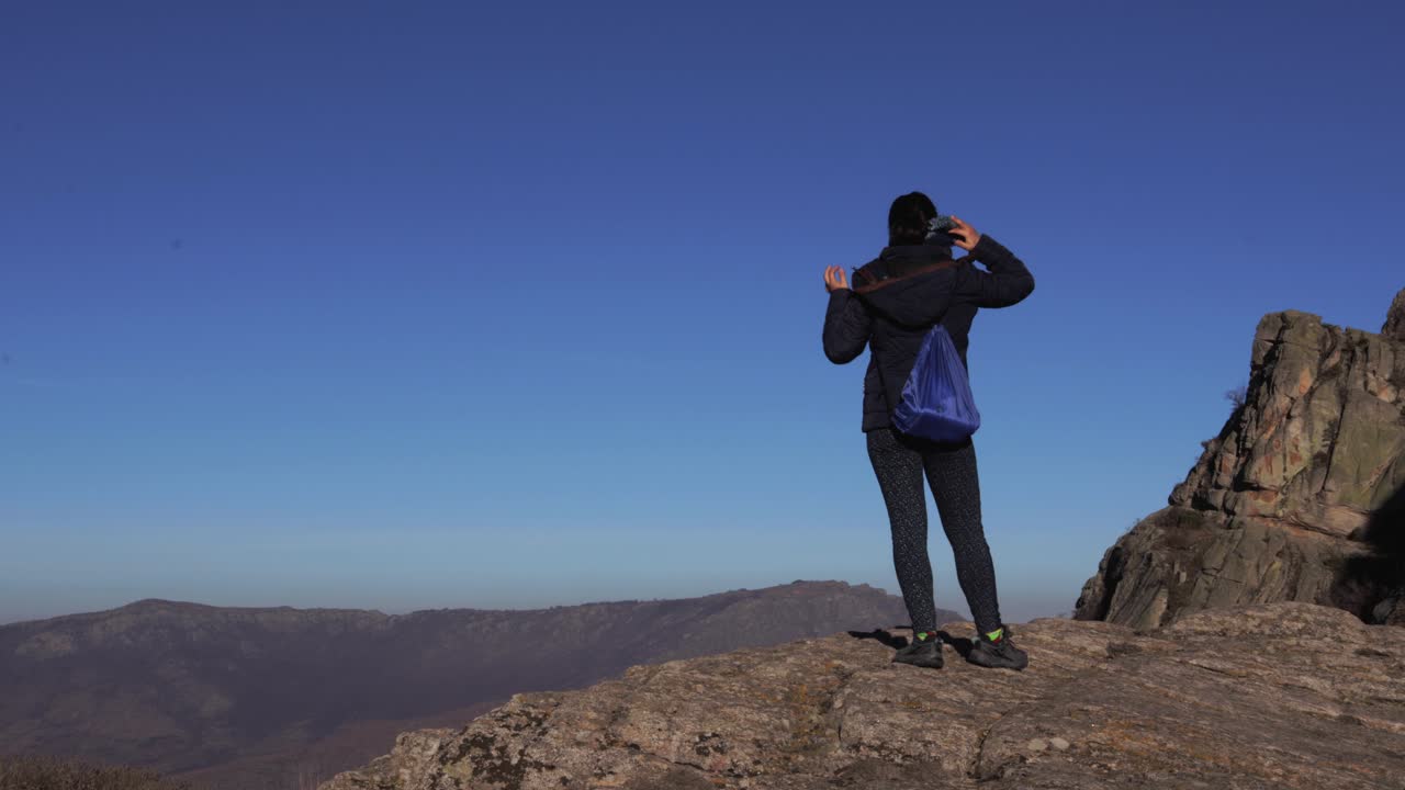una chica solitaria arreglándose la bufanda y el pelo mientras mira una cordillera a lo lejos