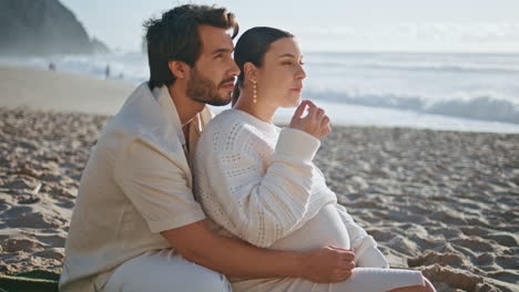 familia embarazada sentada de picnic comiendo bayas frescas en la playa de la noche de cerca