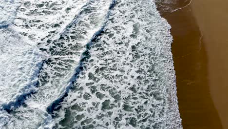 frothy ocean waves washing onto a sandy shore, aerial view