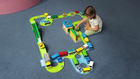 adorable little girl playing with toy cars moving bus on ramp road built highway