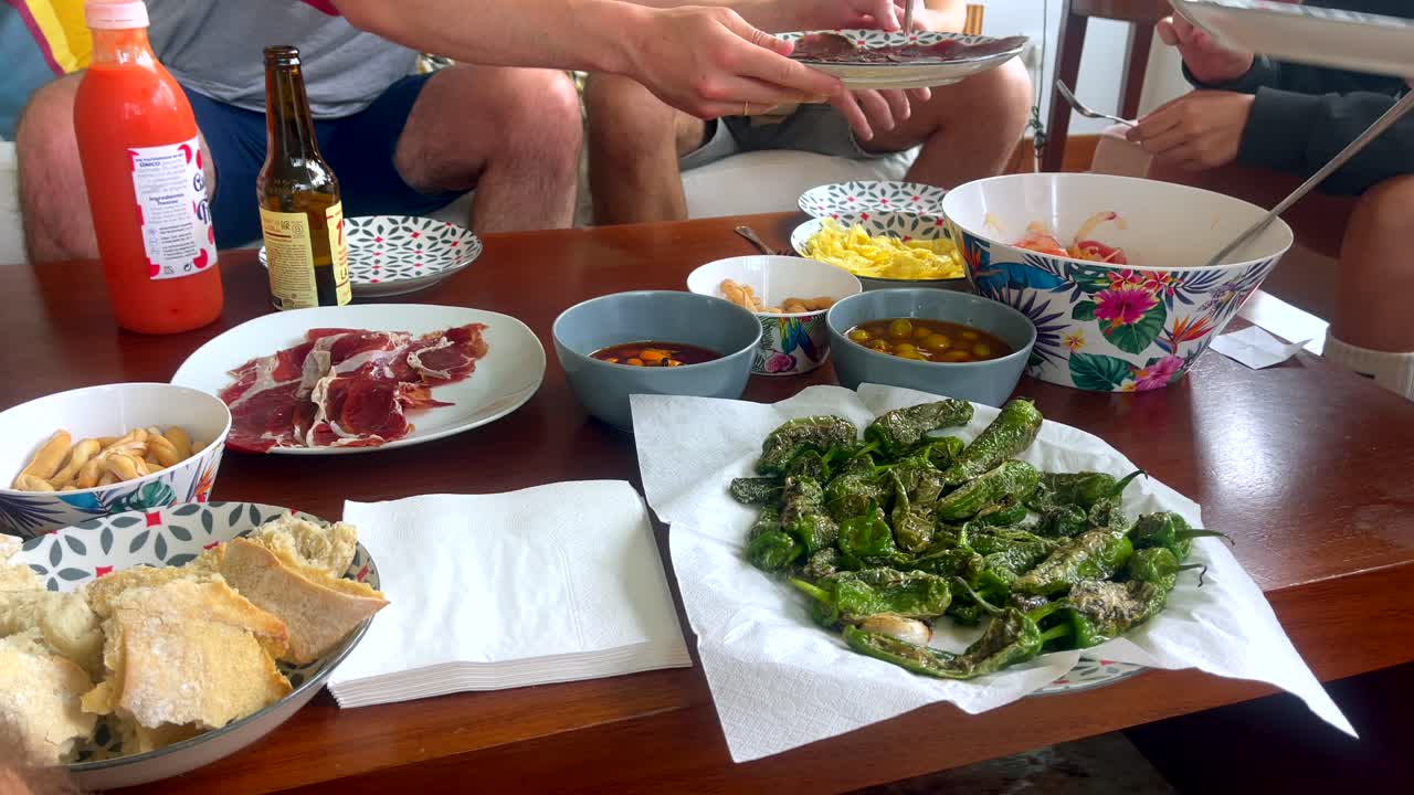 Close-up of Spanish tapas including ham, padrón peppers, and bread at a casual gathering