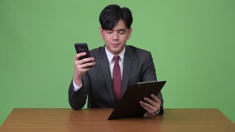젊은 잘생긴 아시아 사업가 녹색 배경에 클립보드와 함께 작업