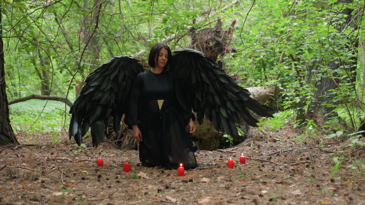 Black forest fairy dressed in flowing dark gown stands before five glowing candles on forest ground, steps forward kneel in quiet devotion, performing sacred prayer to gods