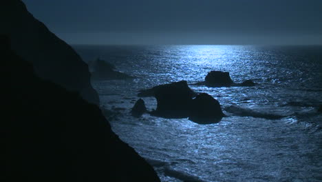 surf rolls into the big sur coastline of california under a full moon effect