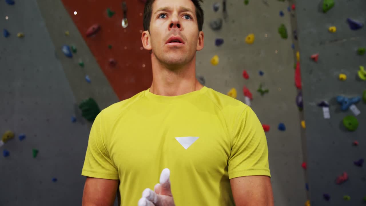 hombre empapando su mano con polvo de tiza antes de escalar la pared artificial 4k