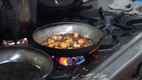 handheld motion shot capturing a chef pan frying salmon bites with onion slices, rapidly tossing, swirling stirring in fast pace commercial kitchen