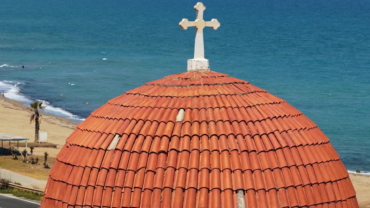 Vista aerea con drone della cupola con tegole rosse e della croce di una chiesa greco-ortodossa sopra una spiaggia sabbiosa, Episkopi, Grecia