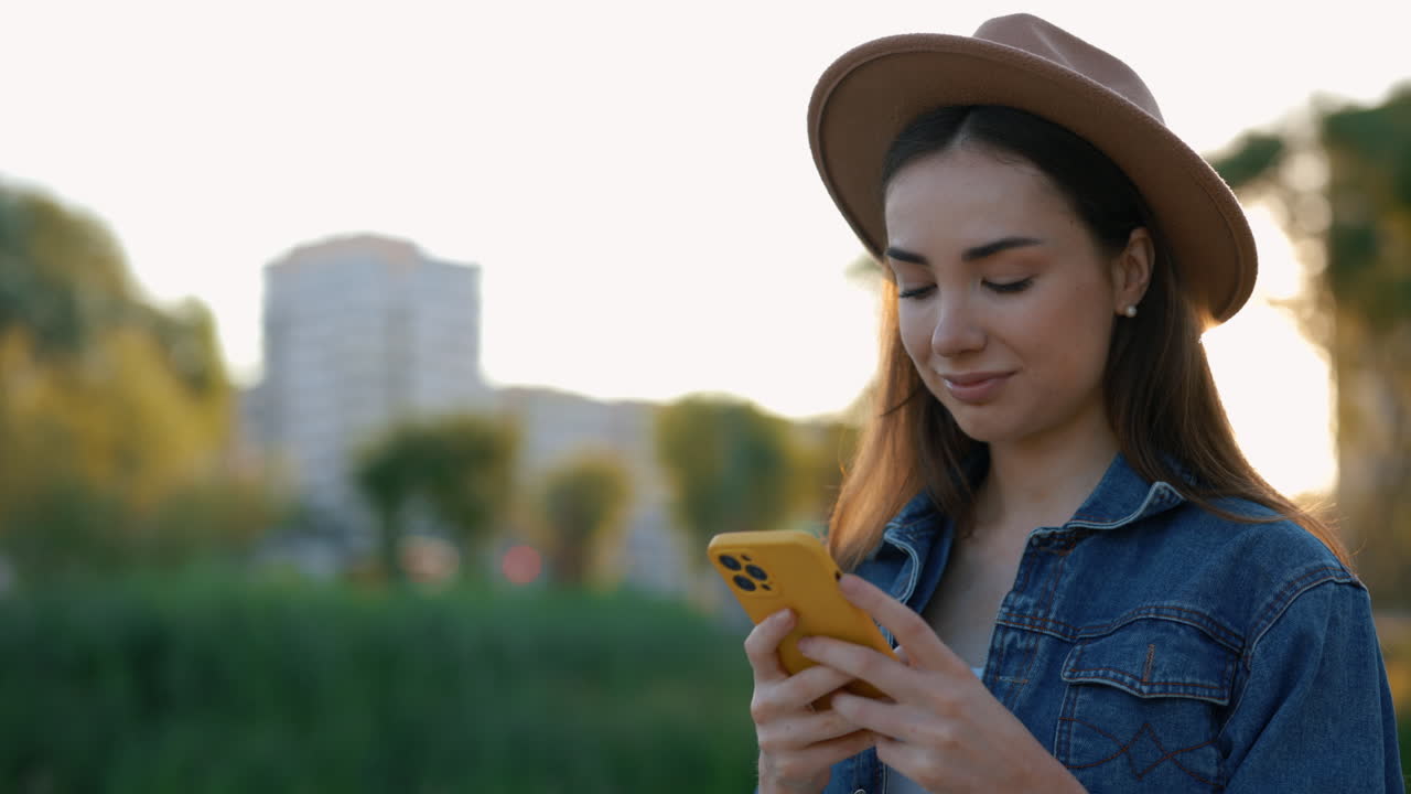 Young Woman Using Phone in Park at Sunset