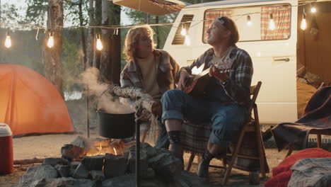 young couple sitting to guitar by campfire