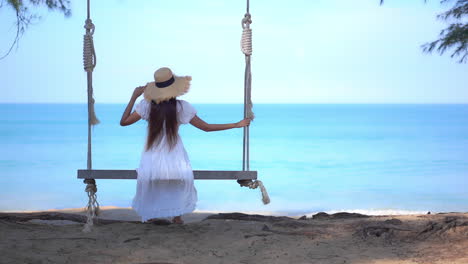 Mujer-Solitaria-En-Columpio-Por-Playa-Tropical-En-Vestido-De-Verano-Y-Sombrero,-Vista-Increíble-Sobre-El-Mar-Azul-Y-El-Horizonte,-Marco-Completo