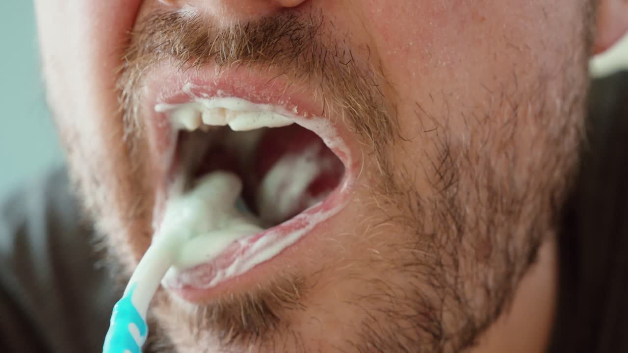 Close-up of a man brushing his back teeth with a toothbrush and toothpaste