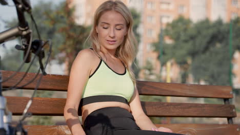 Mujer-Atleta-Feliz-Leyendo-Un-Libro-Sentado-En-Un-Banco-Al-Aire-Libre