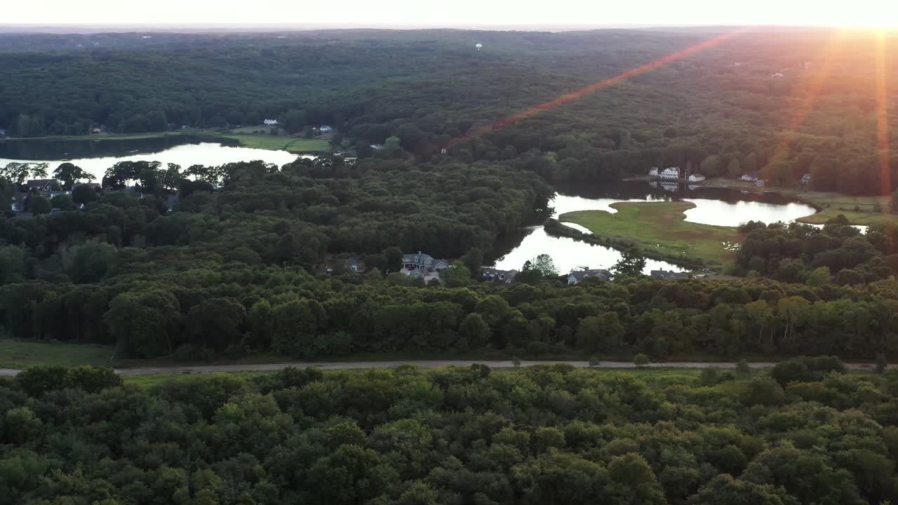 angled aerial flight over a forested area of the Northeastern USA reveals the summer sunset, with lens flare