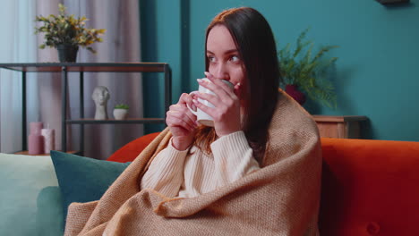 Portrait-of-smiling-young-adult-woman-in-warm-white-sweater-drink-hot-beverage-mug-relaxing-at-home