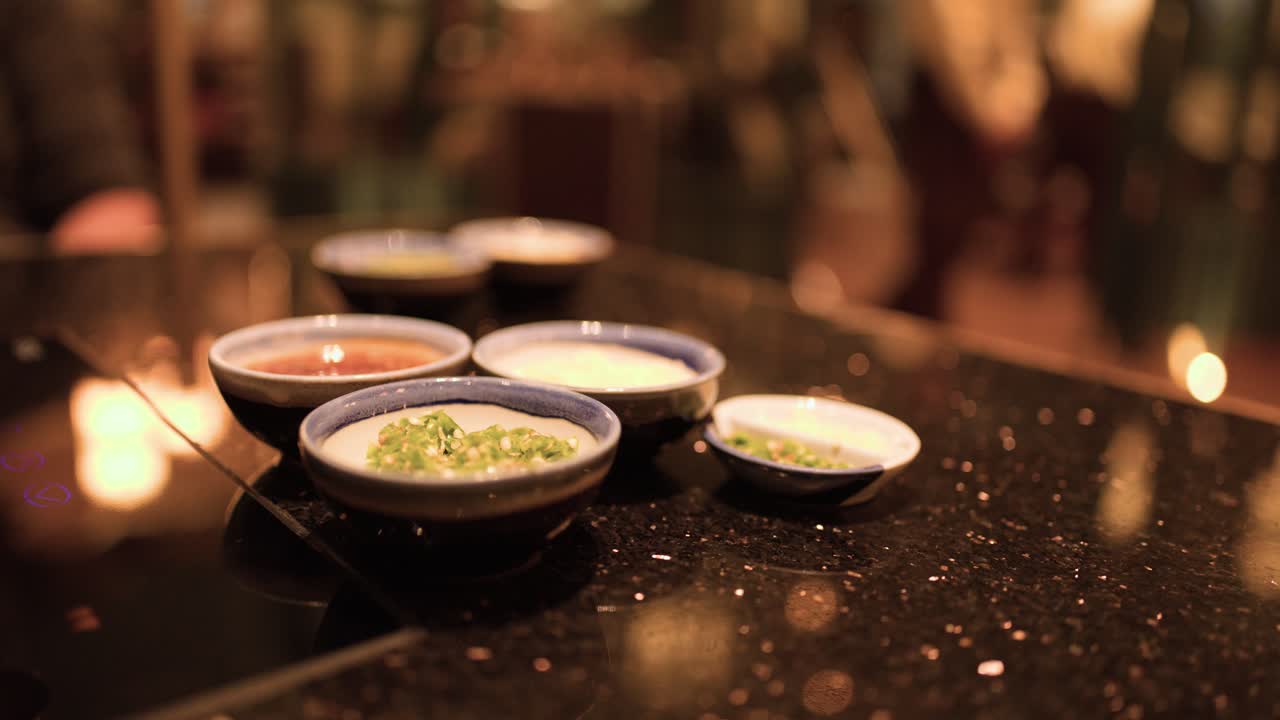 Hand reaches for assorted Asian dipping sauces in small bowls on glossy restaurant table
