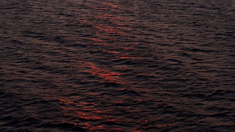 beautiful sunset red light dances on wave tops of ocean water surface, aerial dolly