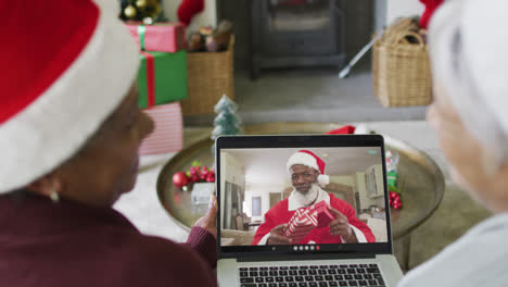 Diverse-senior-female-friends-using-laptop-for-christmas-video-call-with-happy-santa-on-screen