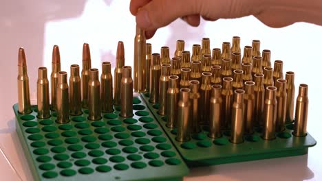 Hand-picking-up-empty-brass-rifle-casings-from-tray-to-add-gunpowder---Static-closeup-of-tray-with-both-empty-casings-and-ready-ammunition-with-bullet