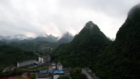 Pull-back-aerial-shot-of-Yangshuo-green-mountains-at-edge-of-city,-covered-by-fog-early-in-the-morning