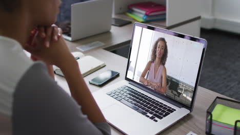mujer de negocios afroamericana sentada en un escritorio usando una computadora portátil haciendo una videollamada con una colega