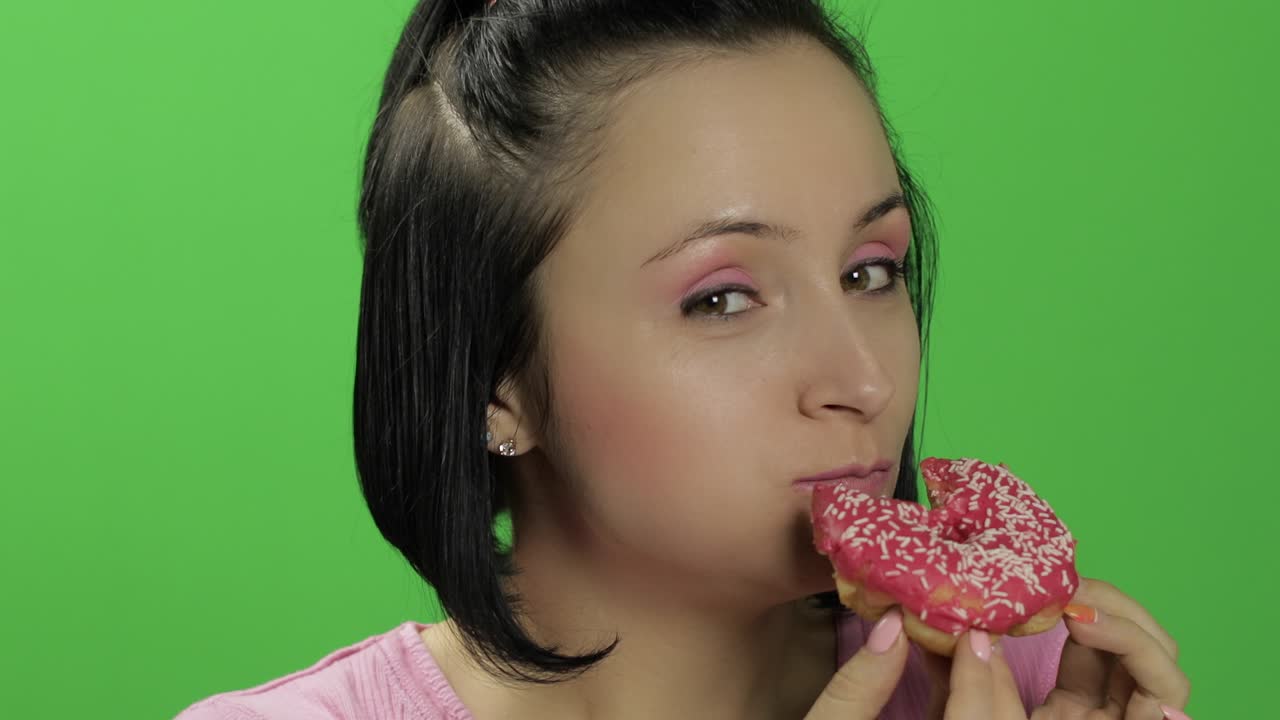 Beautiful young woman with great pleasure eats a donut. Chroma key