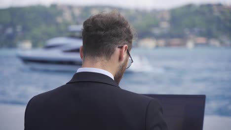 Businessman-working-on-laptop-against-the-sea.