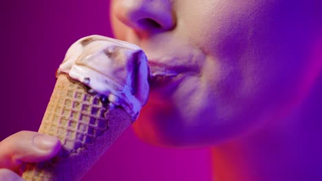 close up of a young pretty woman eating a vegan ice cream with vegan chocolate and enjoying the delicious taste in front of purple background in slow motion