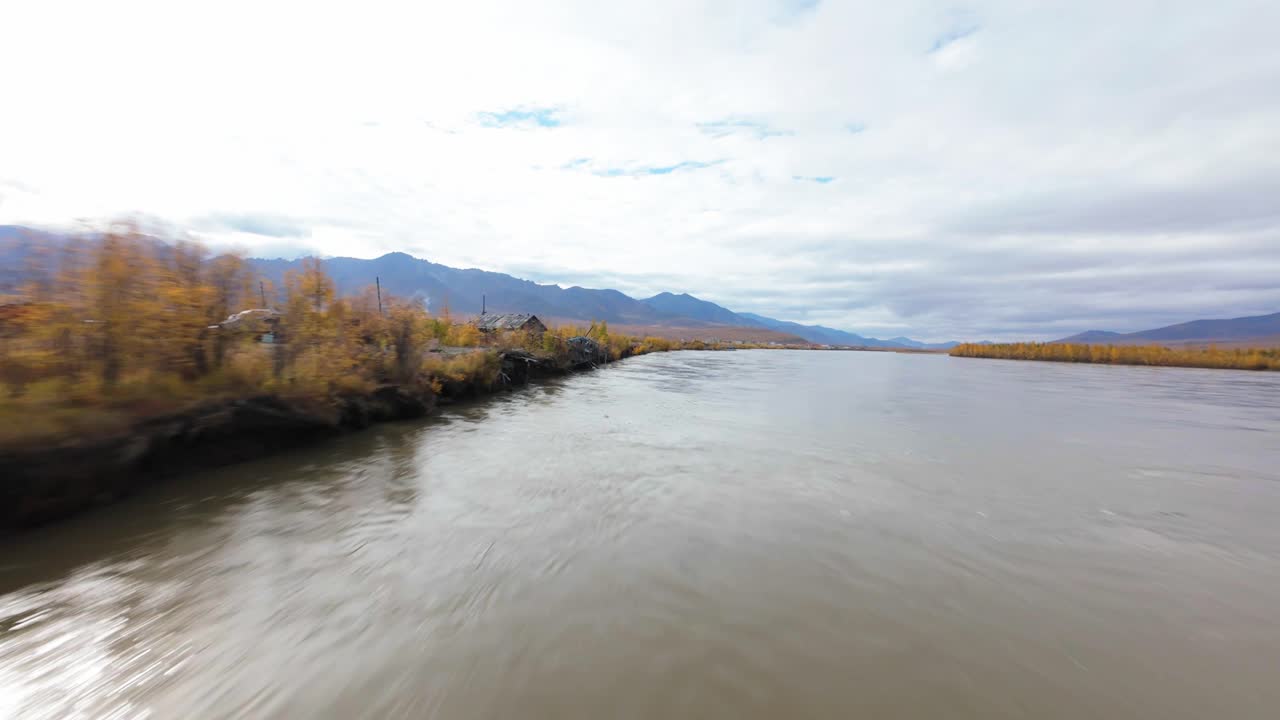 Experience the tranquil beauty of a winding river flanked by vibrant autumn leaves, captured from the sky. The landscape reveals stunning hues of gold and green under a gentle gray sky.
