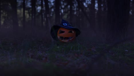 zoom-in-shot-of-a-pumpkin-with-Halloween-hat-and-broomstick-in-the-forest-with-fog-all-around