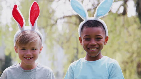 Porträt-Von-Kindern-Mit-Hasenohren-Bei-Der-Ostereiersuche-Im-Garten