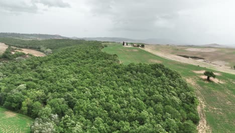 Volando-Sobre-La-Exuberante-Naturaleza-Verde-Hacia-La-Capilla-De-La-Madonna-Di-Vitaleta-En-El-Sur-De-Toscana,-Italia