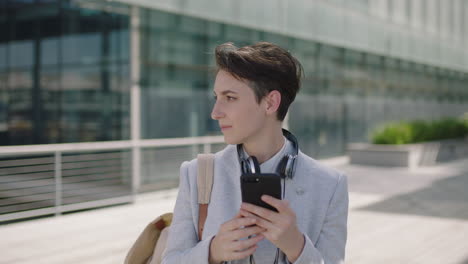 portrait-of-beautiful-young-business-woman-commuter-texting-browsing-using-smartphone-social-media-app-relaxed-wearing-backpack-leaving-work-in-city