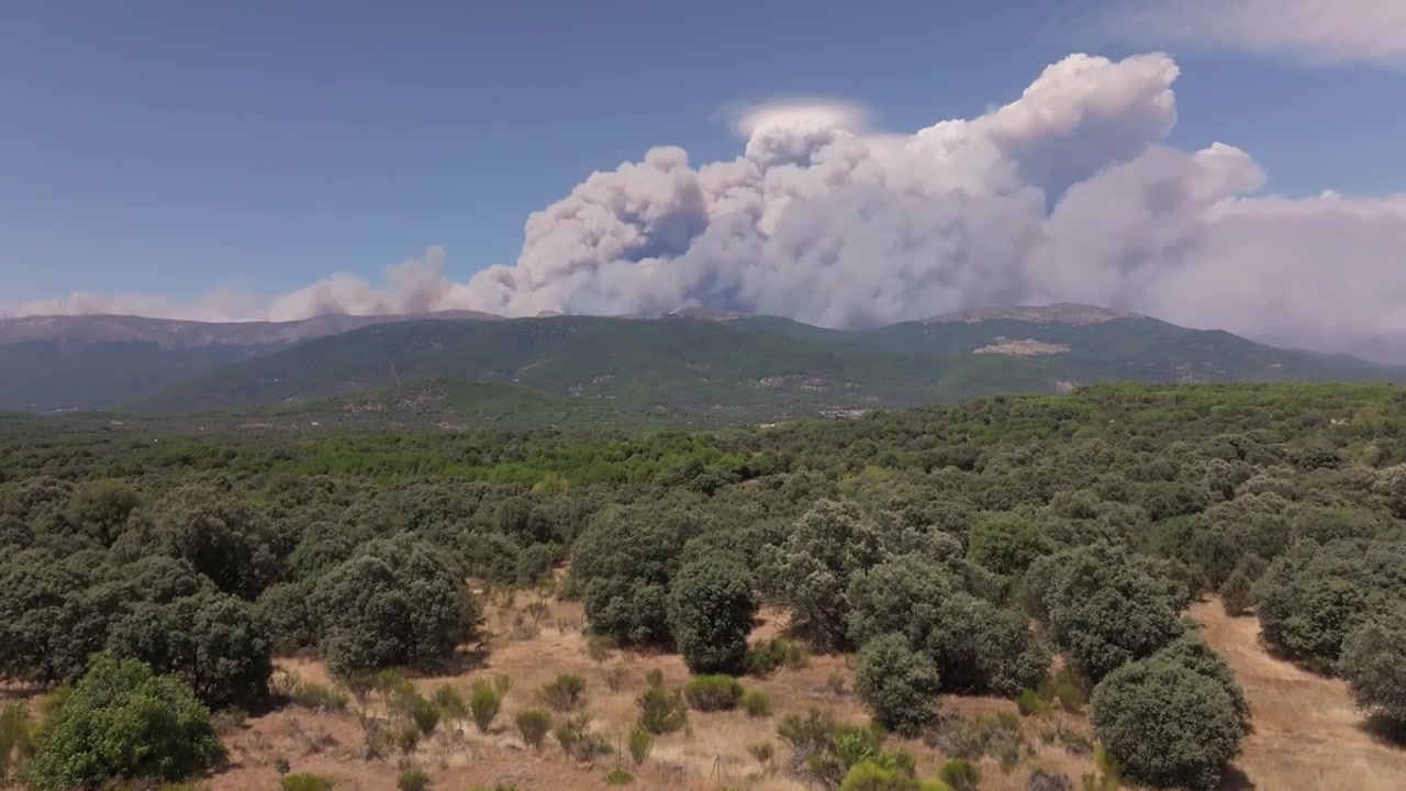 Vista aerea ascendente da drone sulla Valle del Tiétar che mostra un'enorme nube pirocumulo che si innalza sopra il lato settentrionale della Catena Montuosa Centrale, generata da un intenso incendio boschivo.