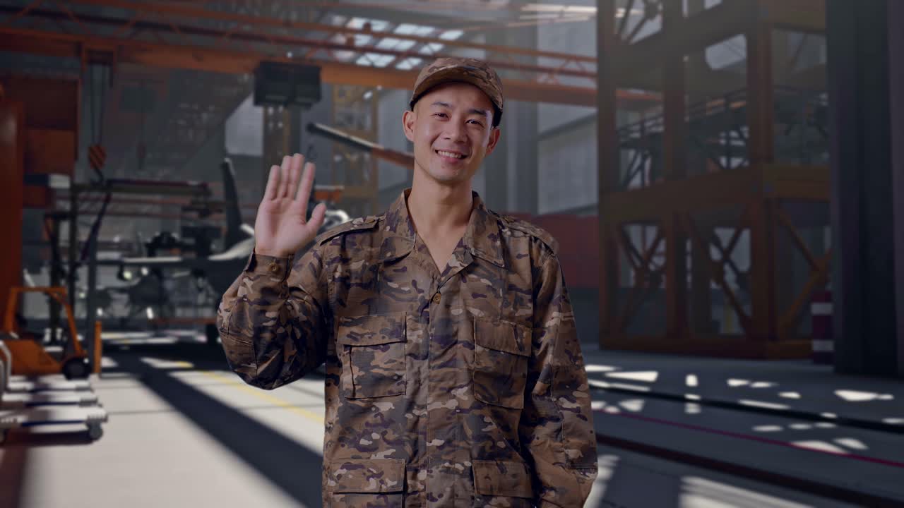 Soldato asiatico sorridente in uniforme mimetica che saluta con la mano