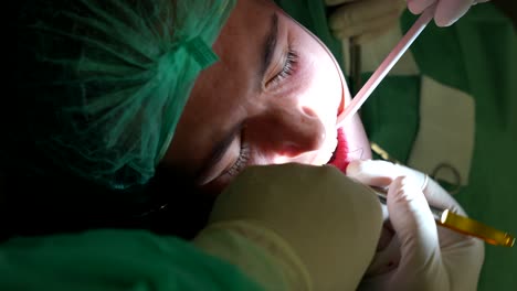 dentista que usa hilo de coser para coser las encías de las pacientes femeninas durante la cirugía dental. de cerca, vertical