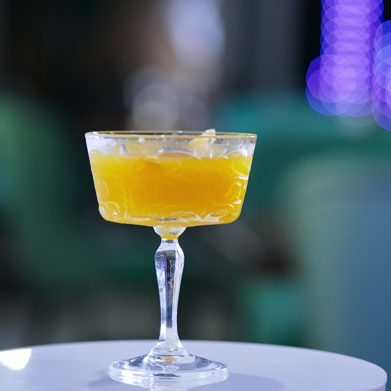 Glass goblet with savory drink. Orange alcohol cocktail on the rotating table. Close up. Blurred backdrop