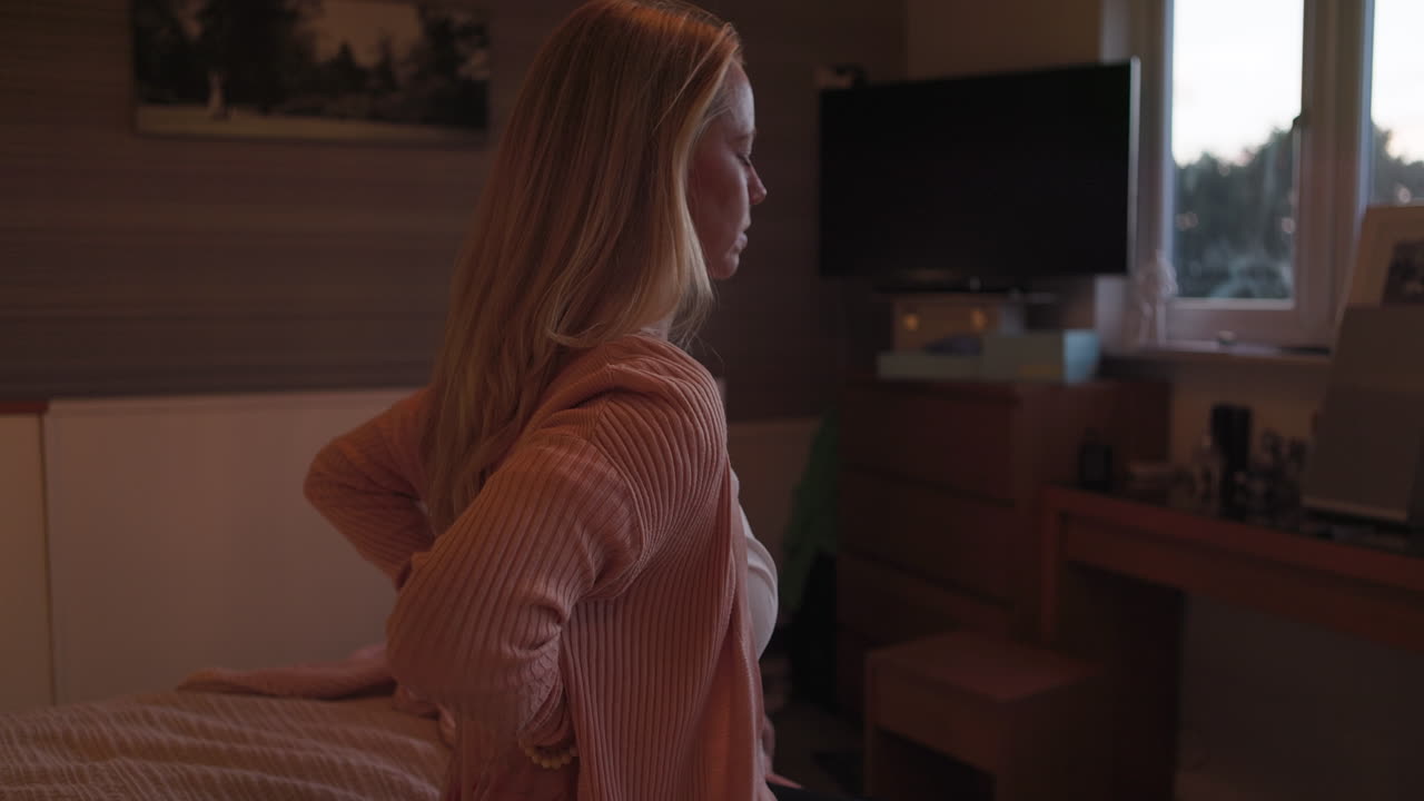 Woman sitting on bed with back pain in bedroom