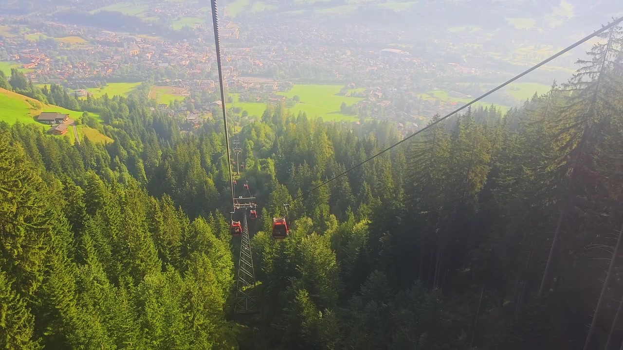 Vista dalla funivia di Kitzbühel in Austria, che domina la città tirolese, hotel, prati, foreste sempreverdi e catene montuose durante una soleggiata giornata di vacanza estiva nelle Alpi.