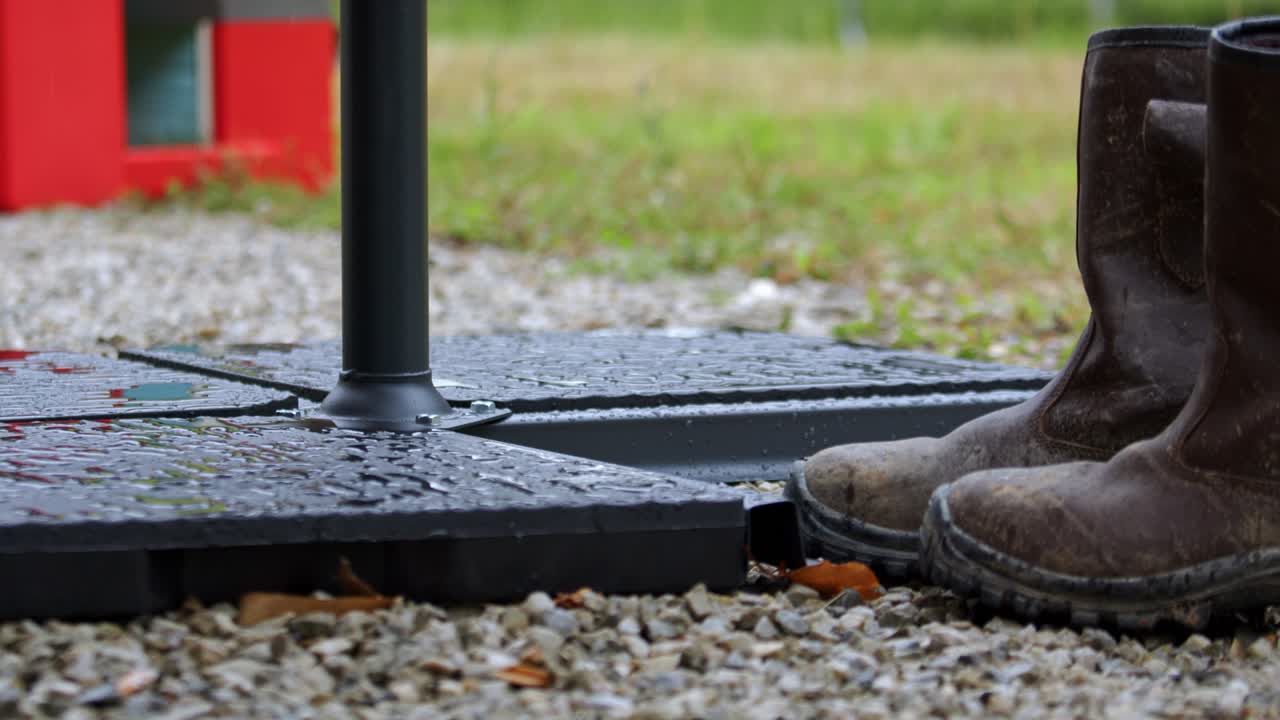 A Pair of Muddy Boots Stands Firmly Beside a Sturdy, Rain-soaked Platform on a Gravel Surface - Close Up