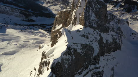 Vista-Aérea-Volando-Sobre-Una-Cresta-De-Montaña-Con-Montañas-En-El-Fondo,-Mientras-Se-Inclina-Hacia-Abajo-Para-Mirar-La-Cresta-Desde-Arriba-En-Los-Alpes-Franceses-En-Invierno,-Cerca-De-La-Clusaz