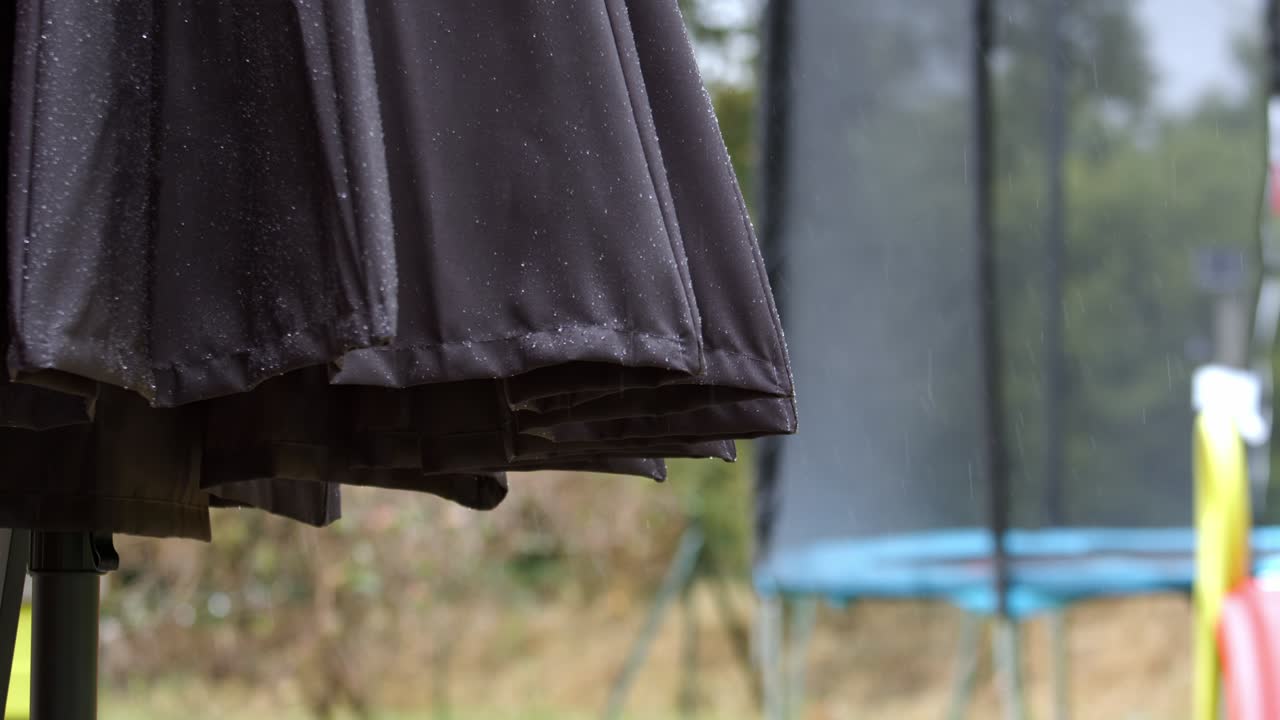 Wet garden umbrella and trampoline during rainfall