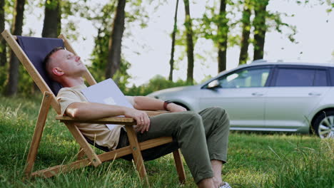 freelancer sleeps in a folding chair with face covered with laptop. tired man having a break from work in the nature.